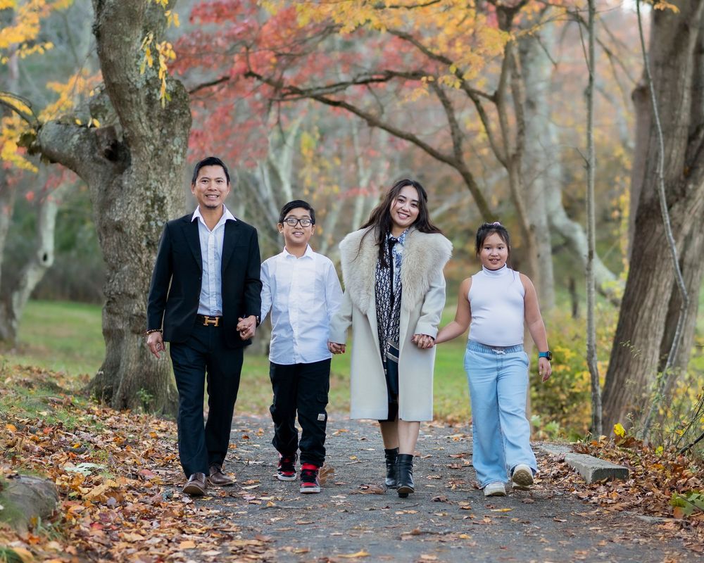 A family of four walks hand-in-hand along a scenic autumn park pathway.Holmdel Park NJ