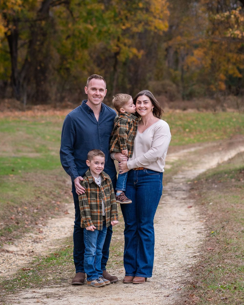 Smiling family of four stands together on a scenic fall nature trail with autumn trees.Middletown NJ