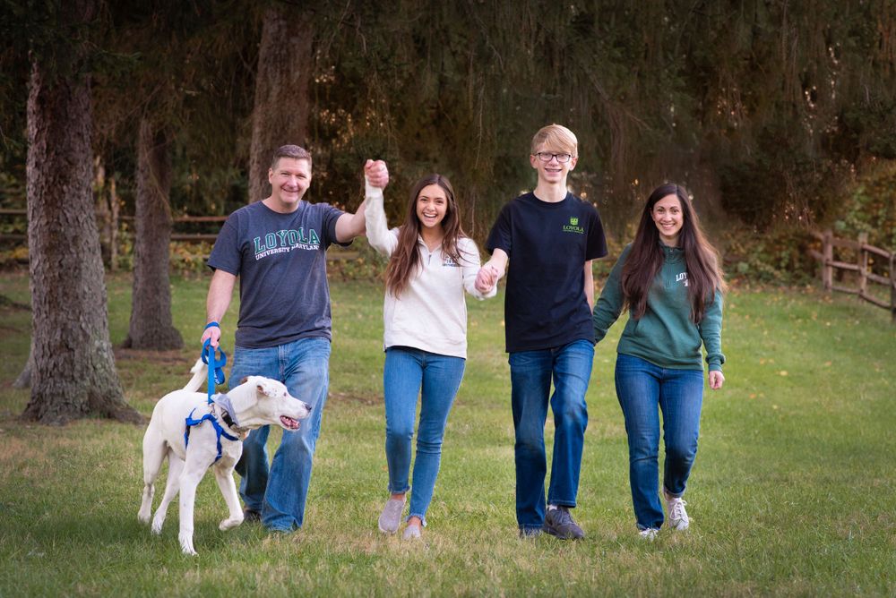 A family and their white dog pose together on grass with evergreen trees in the background.Middletown NJ