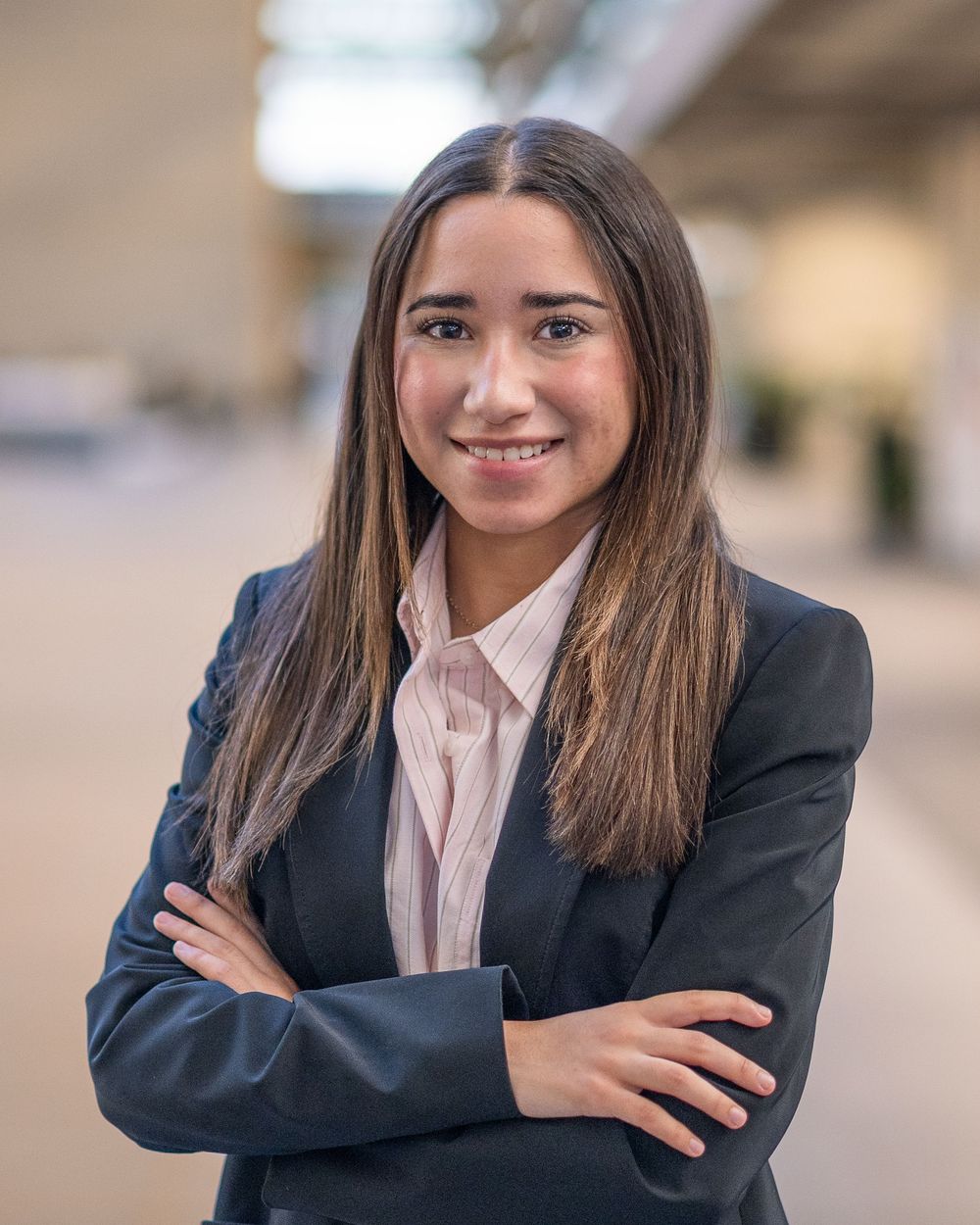 Headshot of Confident young woman in black blazer with arms crossed smiling in a bright indoor setting. Monmouth County NJ
