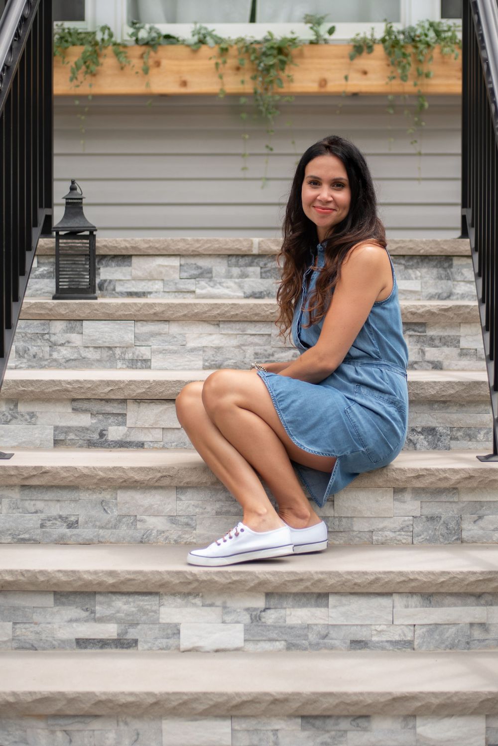 branding portrait of a woman in denim dress sitting on stone steps with lantern and greenery. Middletown NJ