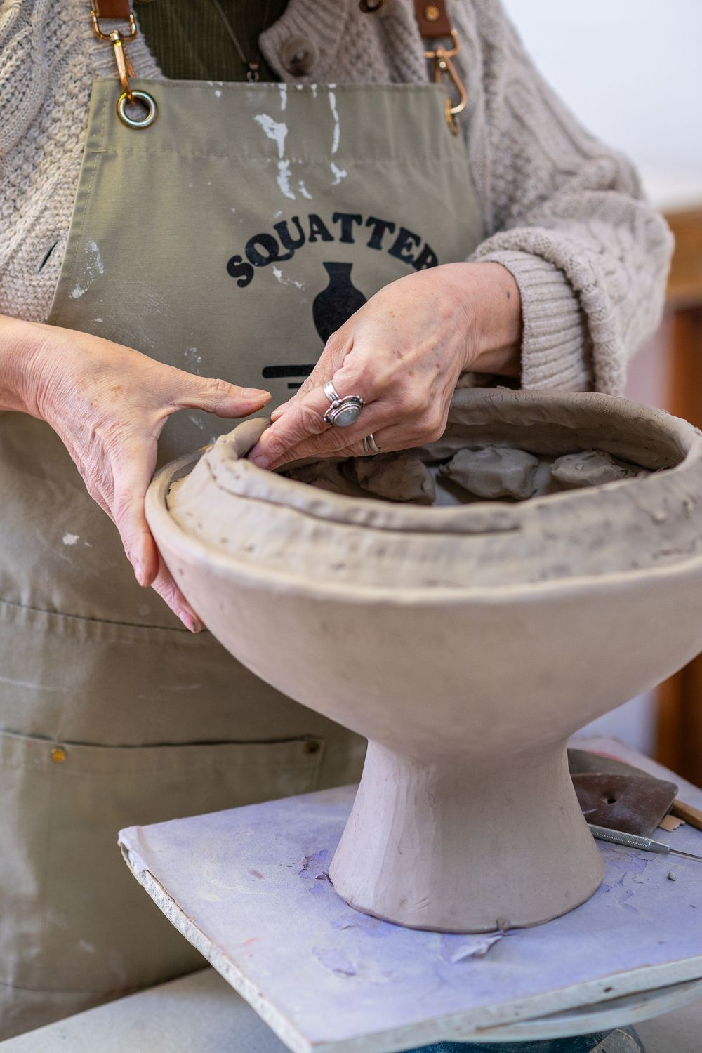 Close-up of hands shaping clay vessel on pottery wheel wearing Squatter Potter apron.Red Bank NJ