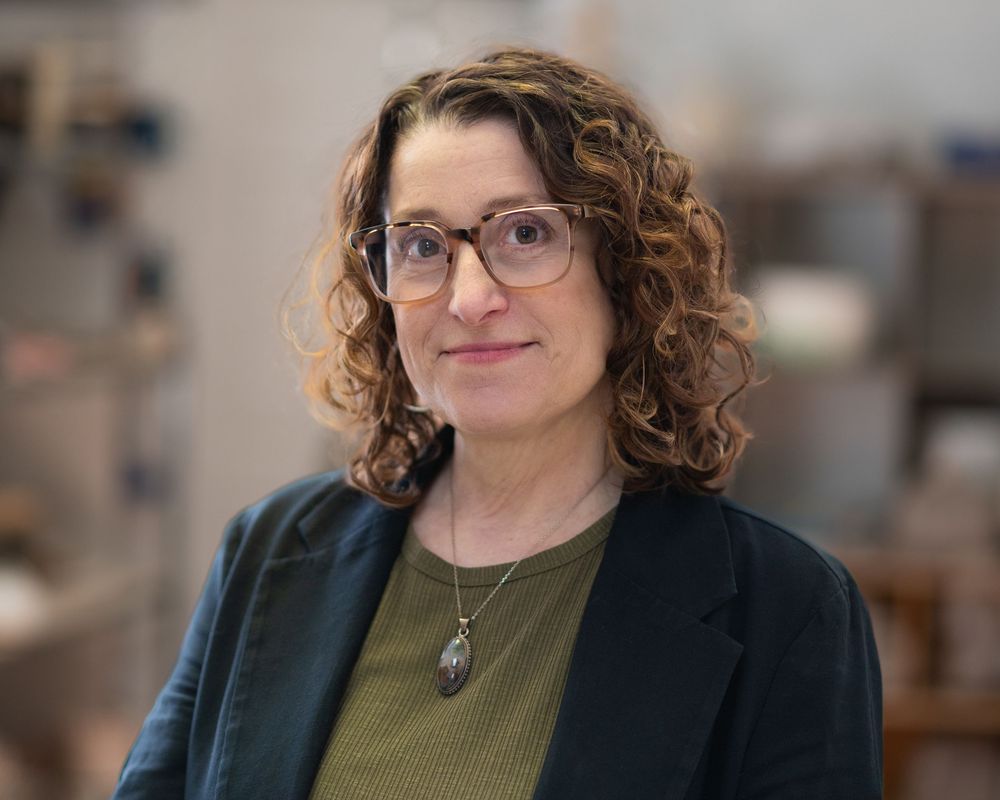 Headshot of Woman with curly hair and glasses wearing a blazer poses for a professional portrait indoors. Red Bank NJ