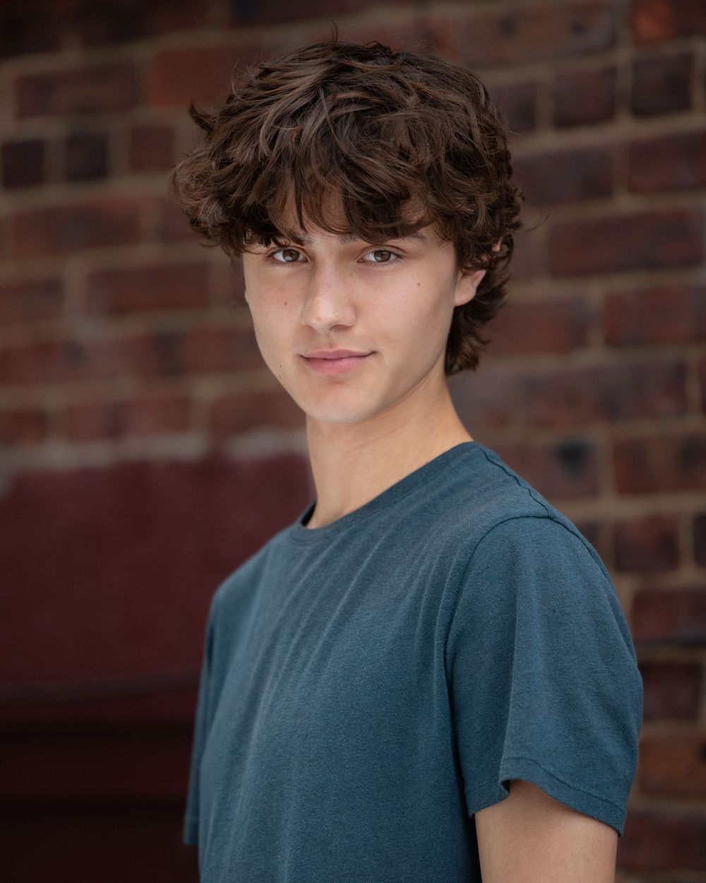 Headshot Portrait of a teen boy in blue shirt against brick background in Atlantic Highlands NJ