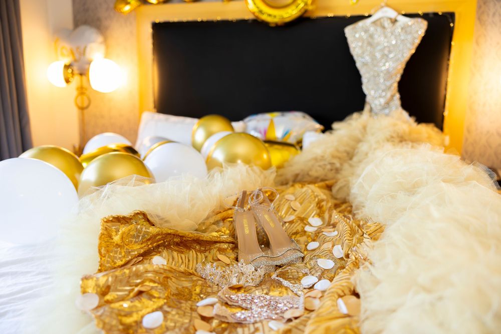 Glamorous wedding dress and accessories laid out on white hotel bed with gold decor.