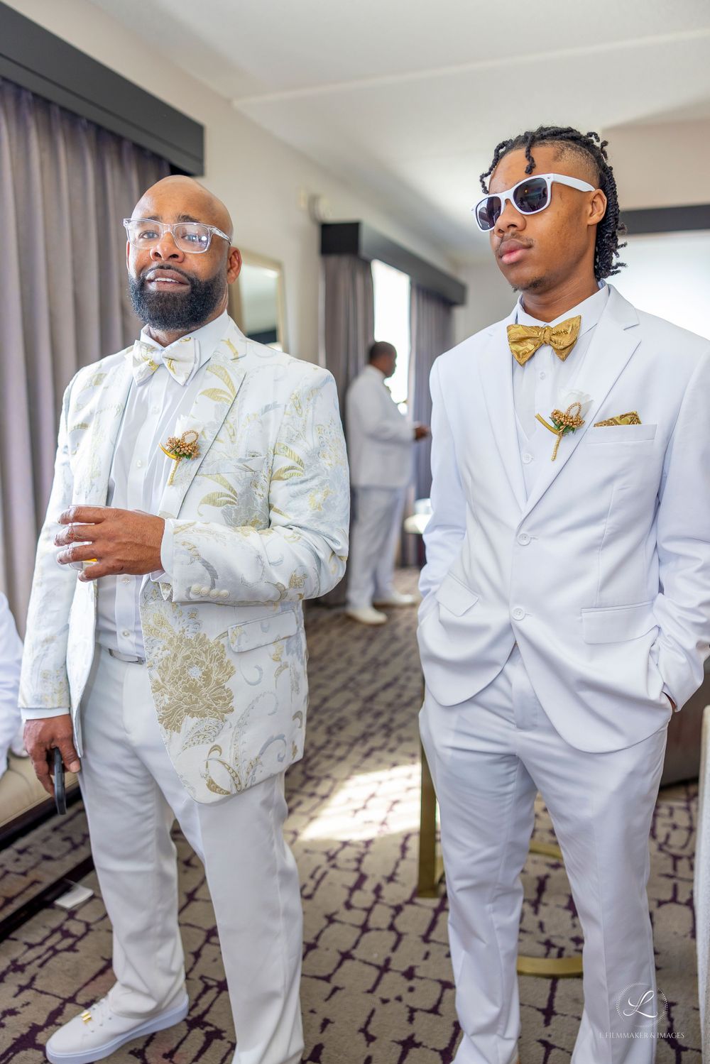 Two people in white suits with gold accents and bow ties standing confidently.