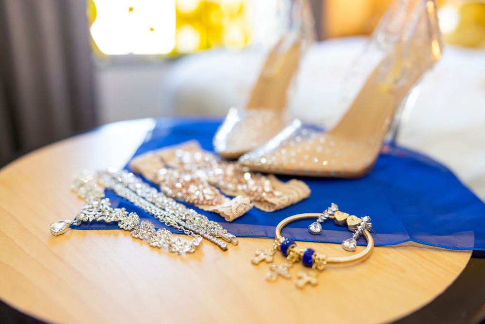 Wedding accessories including blue shoes and jewelry arranged on a beige surface.