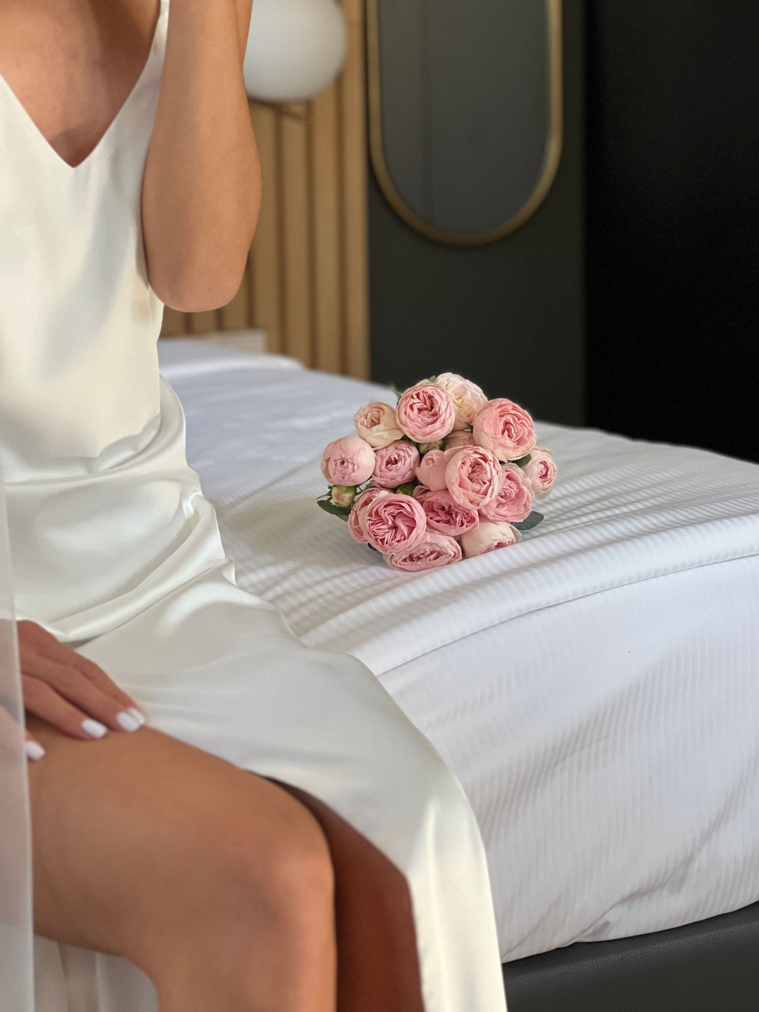 White silk robe and pink roses arranged on bed in bridal boudoir setting.