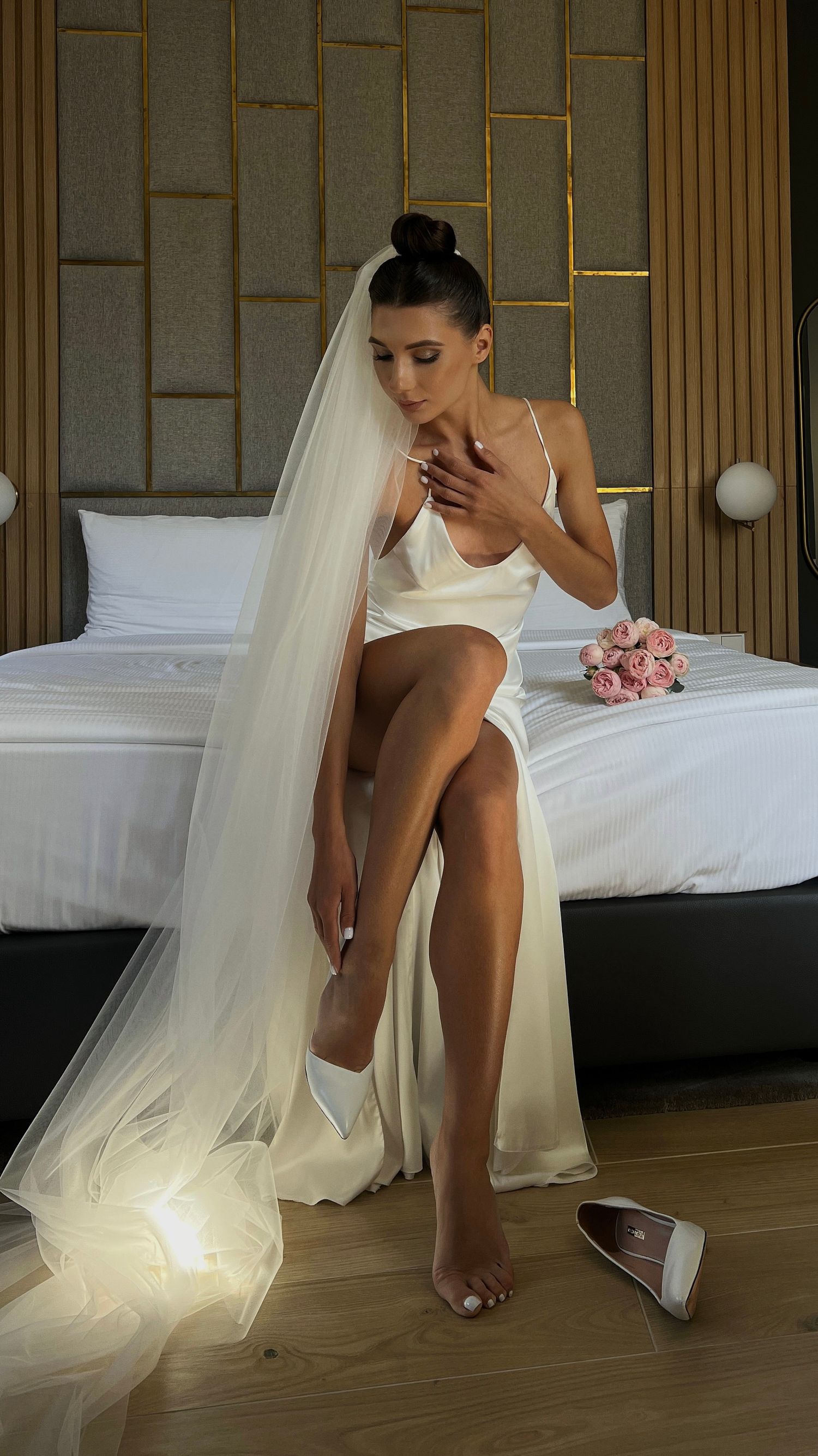 Artistic bridal portrait with dramatic lighting showing white dress and veil on wooden floor.