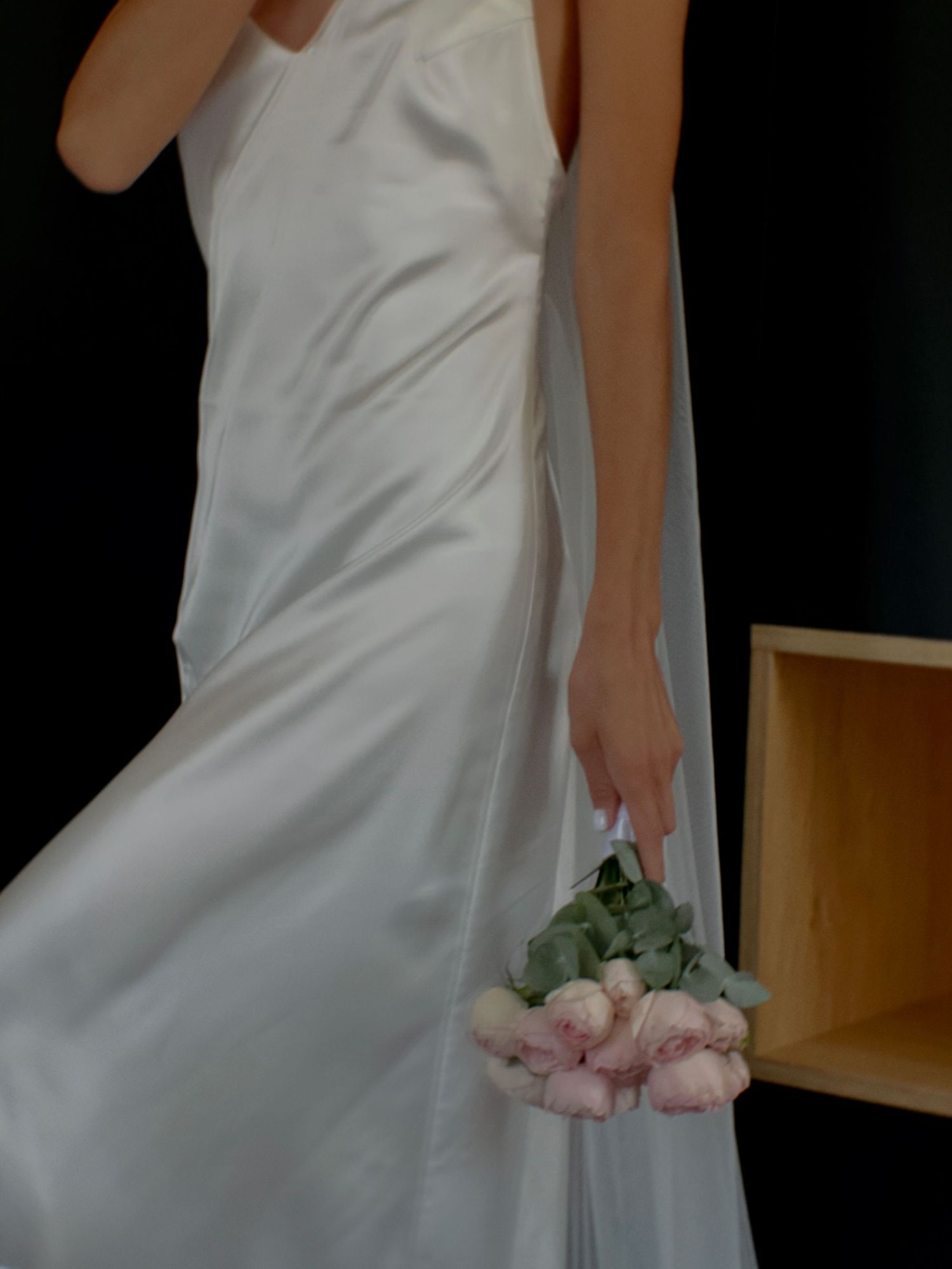 Close-up details of white wedding dress and pink rose bouquet in natural light.