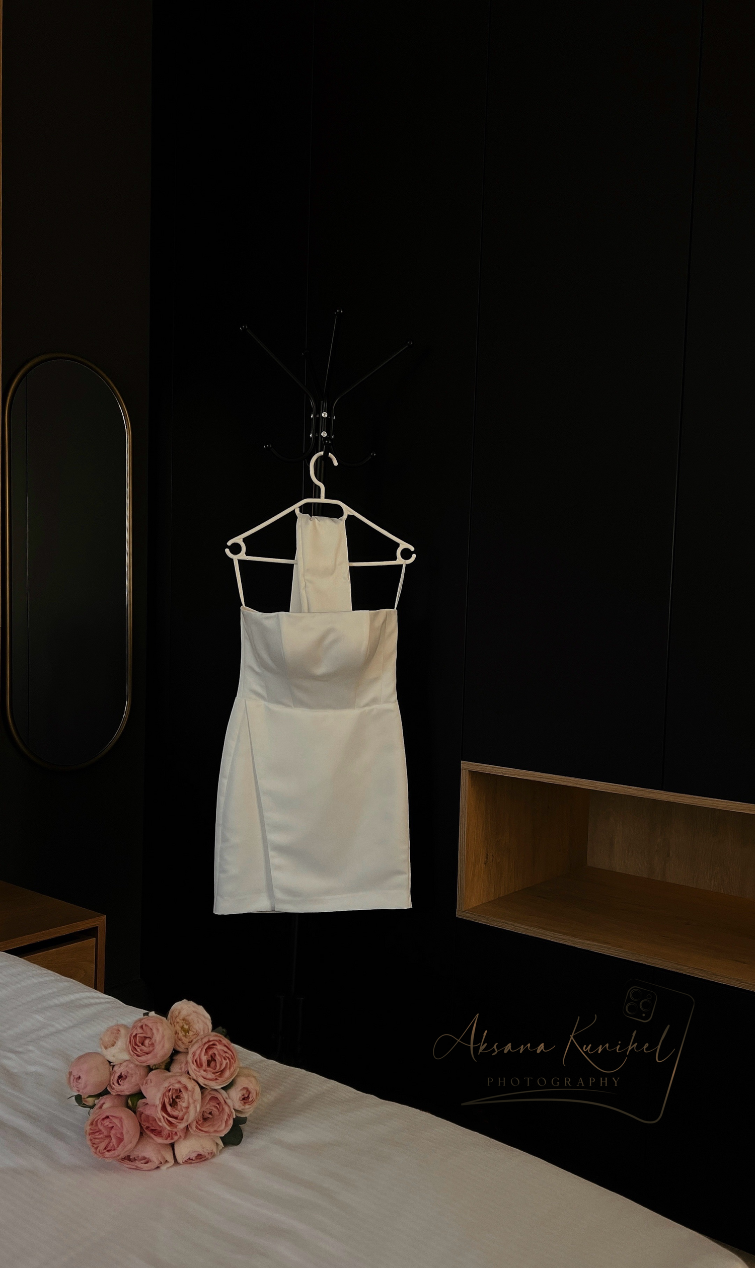 Minimalist white wedding dress hanging against dark wall with pink roses.