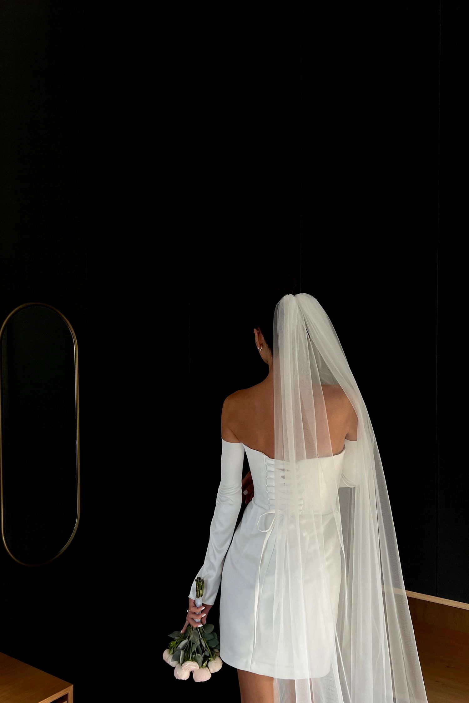 Bride in white dress and veil poses against dark background.