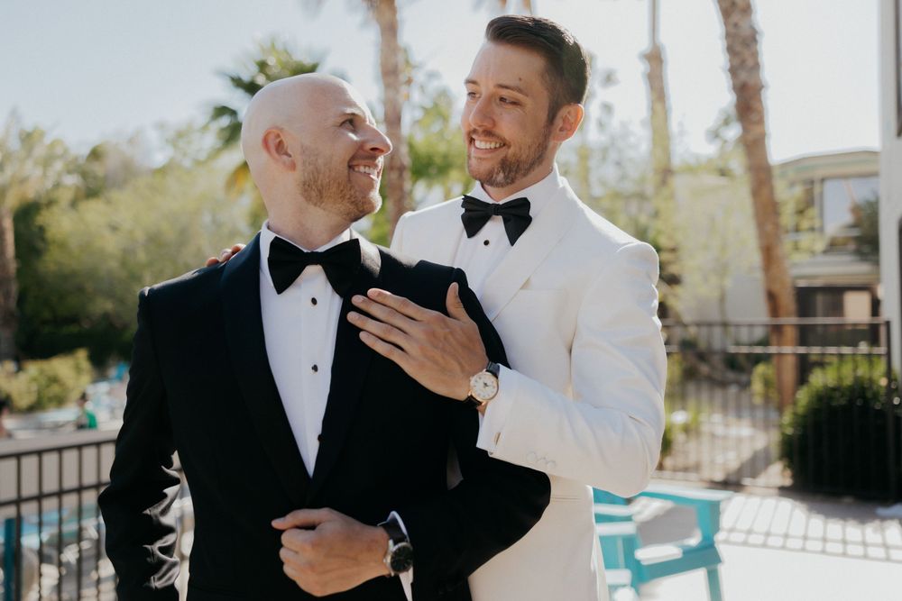 Two people in tuxedos sharing an intimate moment outdoors during a formal event.