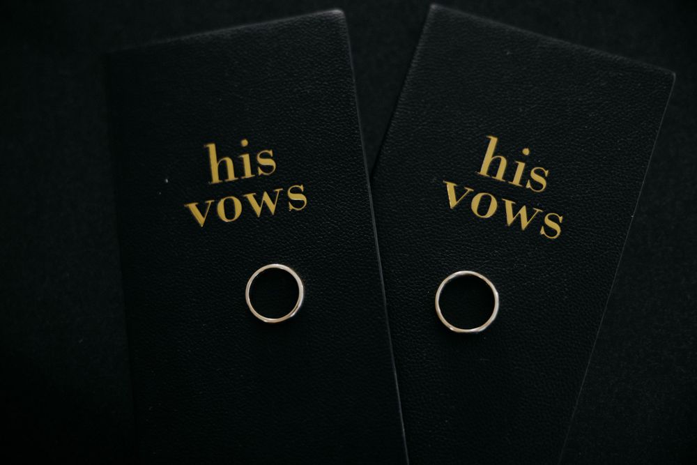 Two matching black vow books with gold text and wedding rings placed on top.