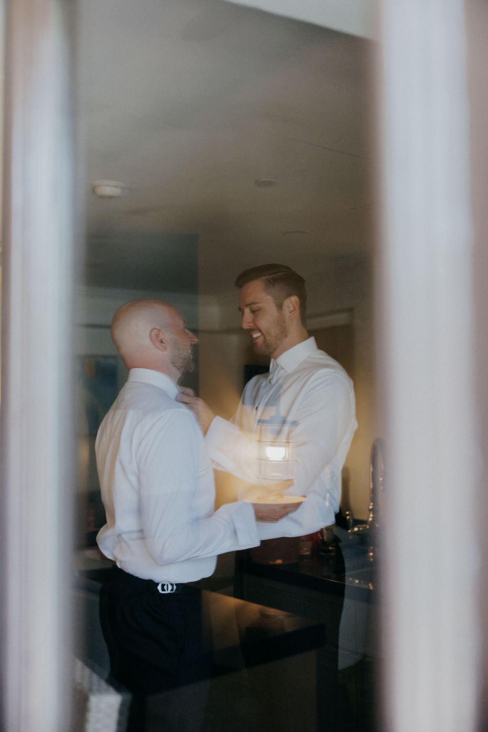 A candid moment captured through glass showing two figures in white shirts getting ready.