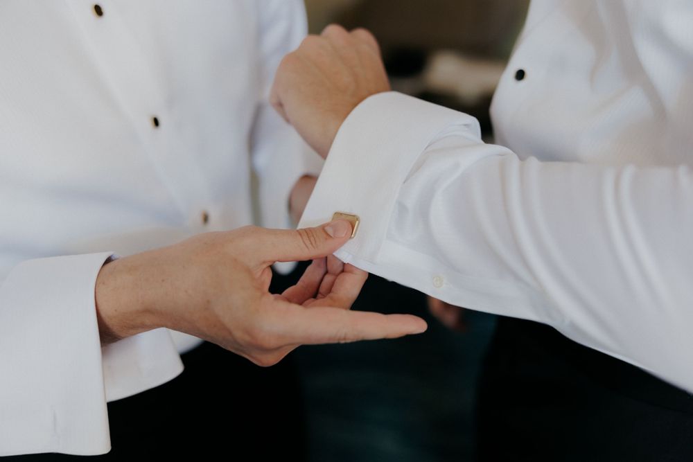 Close-up of hands adjusting formal white shirt cuffs during wedding preparations.