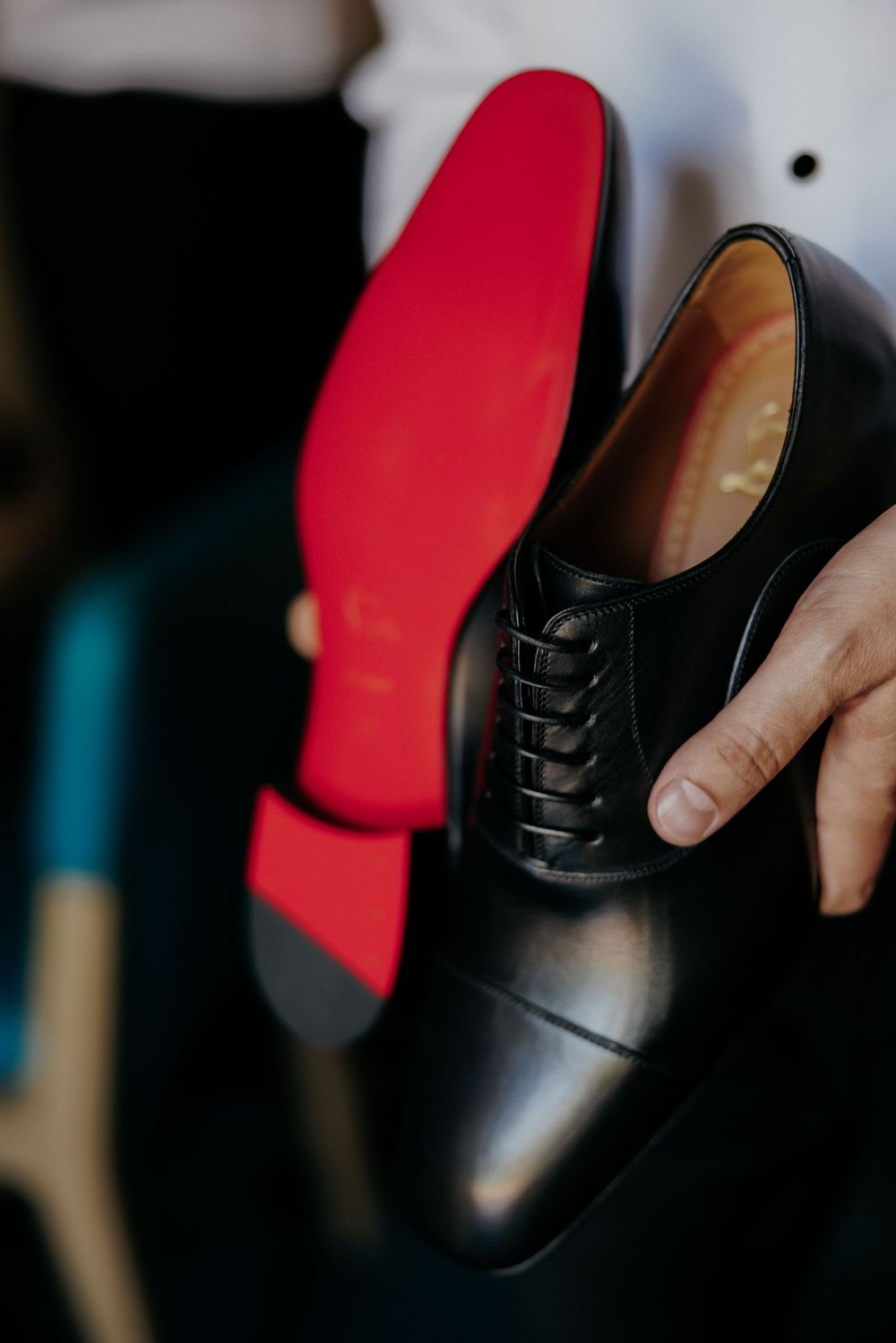 Elegant black leather dress shoe with distinctive red sole being held for display.