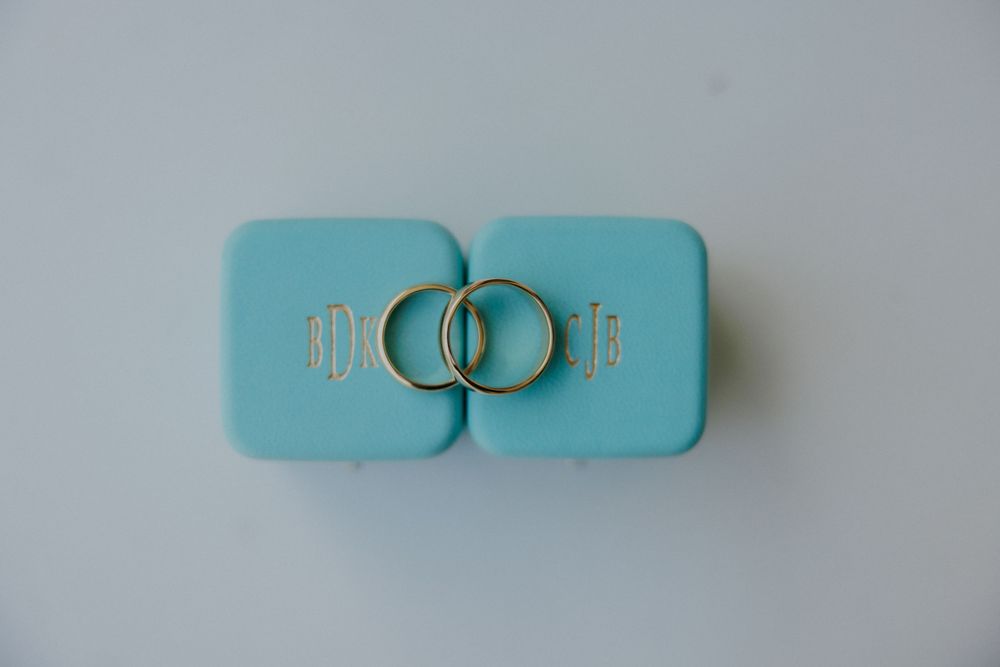 Two teal ring boxes with gold wedding bands arranged on white surface.