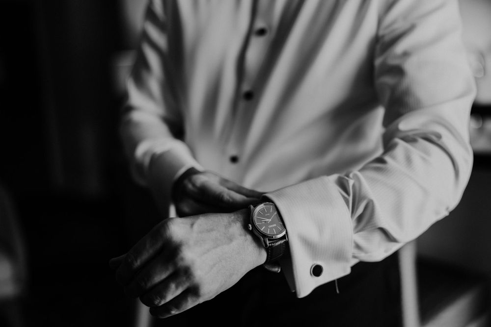 Close-up black and white shot of someone adjusting their watch and formal shirt cuff.