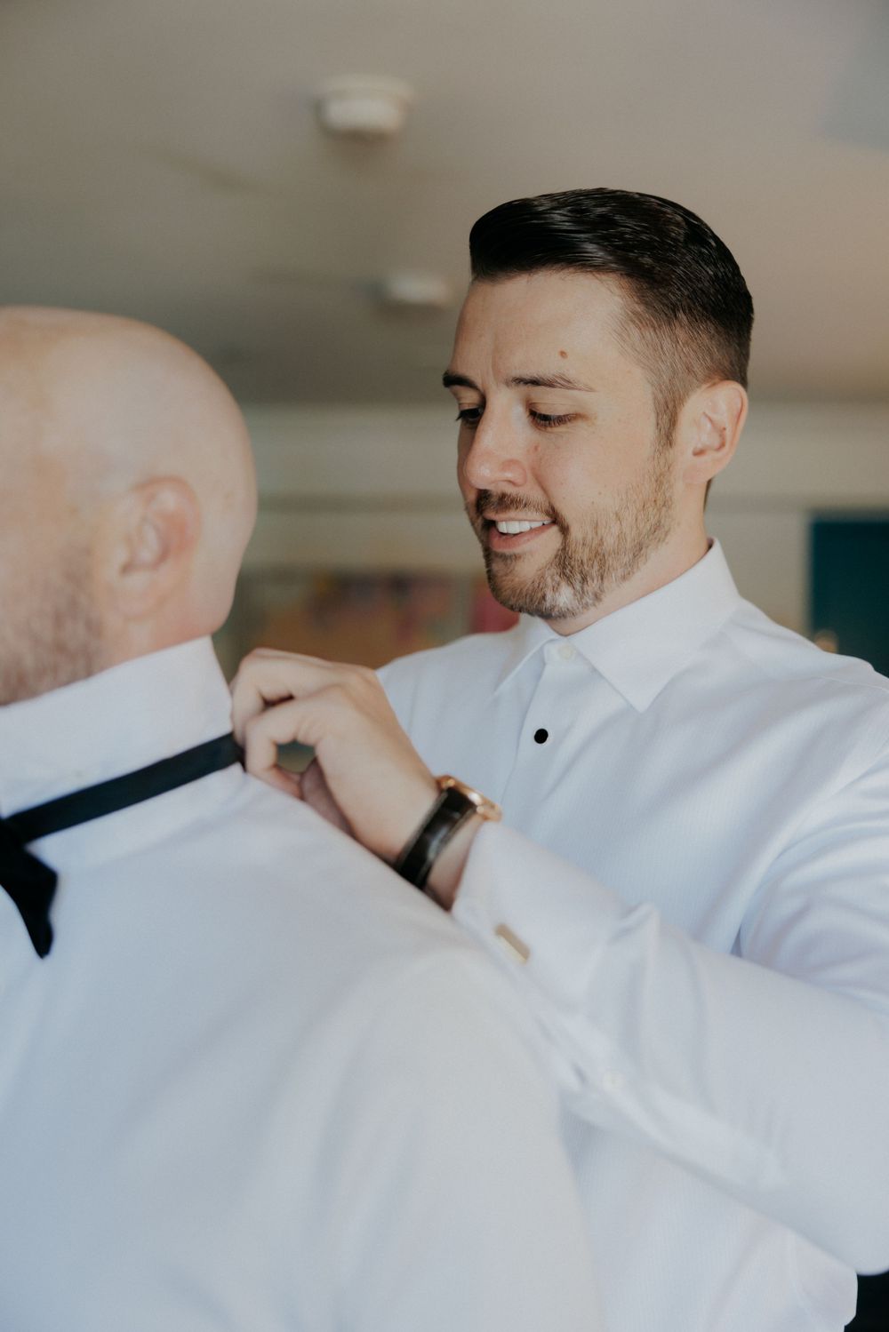A tender moment of bow tie adjustment during wedding preparations.
