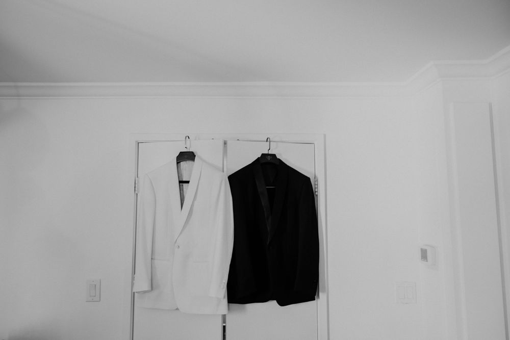 A black and white formal clothing contrast with a black suit jacket and white dress shirt hanging on a wall.