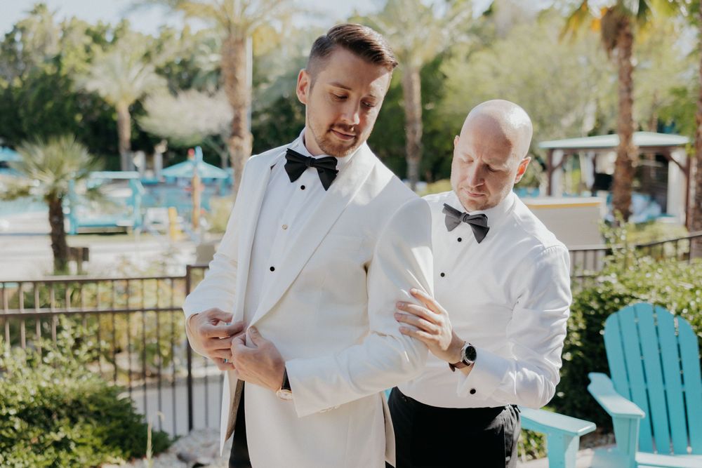 Two people in formal attire sharing a laugh while getting dressed for an event outdoors.