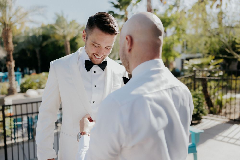 Two people in tuxedos sharing a joyful moment outside on a sunny day.