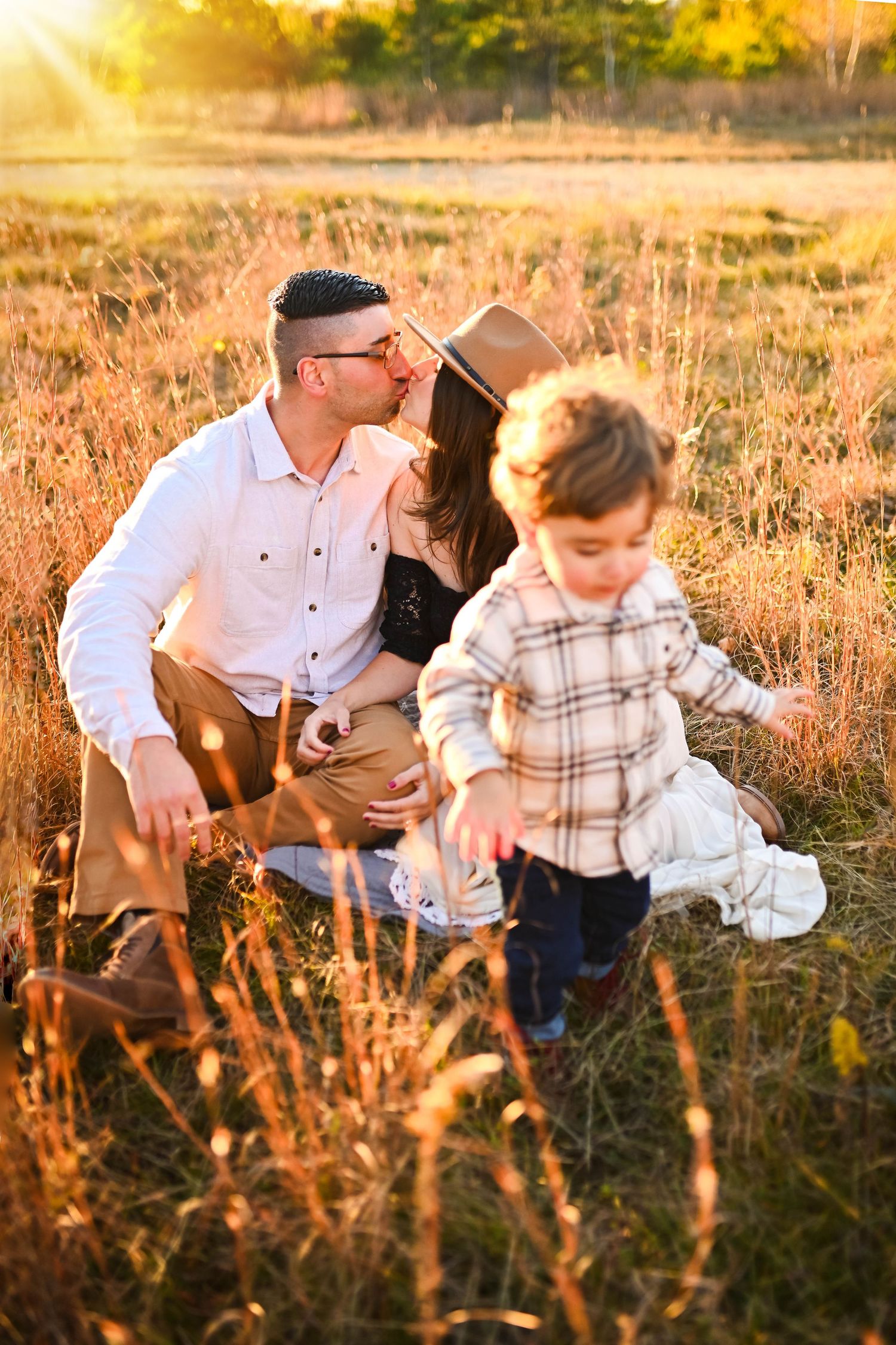 Outdoor family portrait session in tall grass during sunset with warm golden lighting.