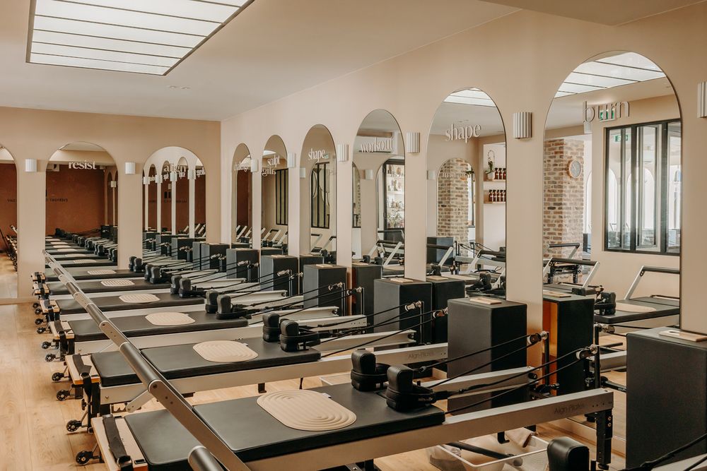 Spacious Pilates studio with rows of reformer machines, arched mirrors, and elegant neutral decor.