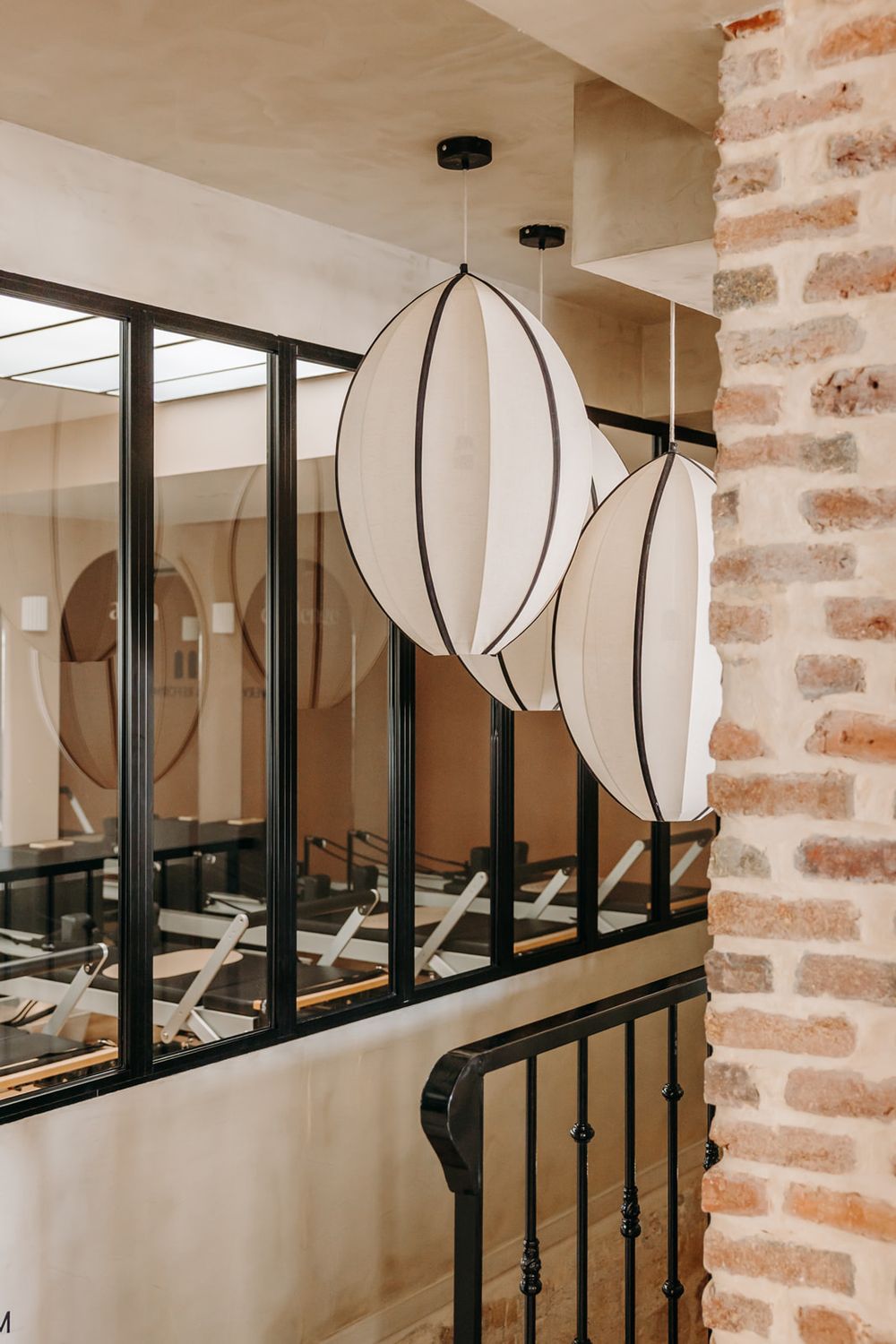 Two white oval pendant lights hang near a brick wall and black-framed glass partition in a modern interior.