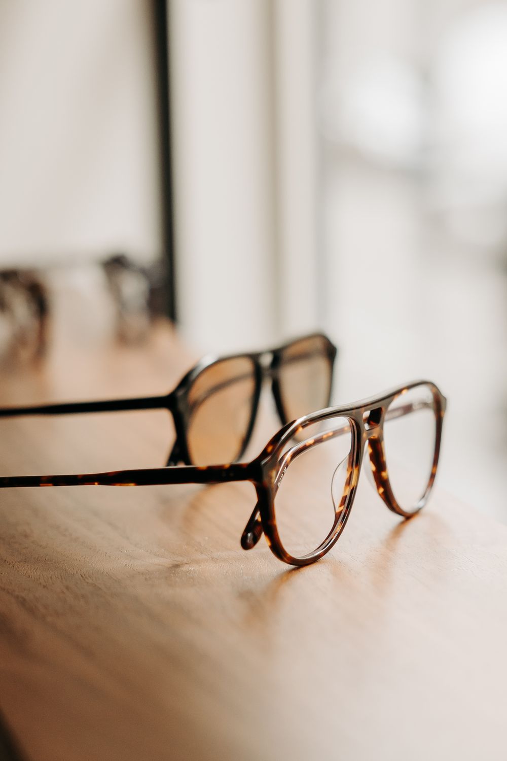 Close-up of tortoiseshell aviator eyeglasses resting on a wooden surface with soft natural light.