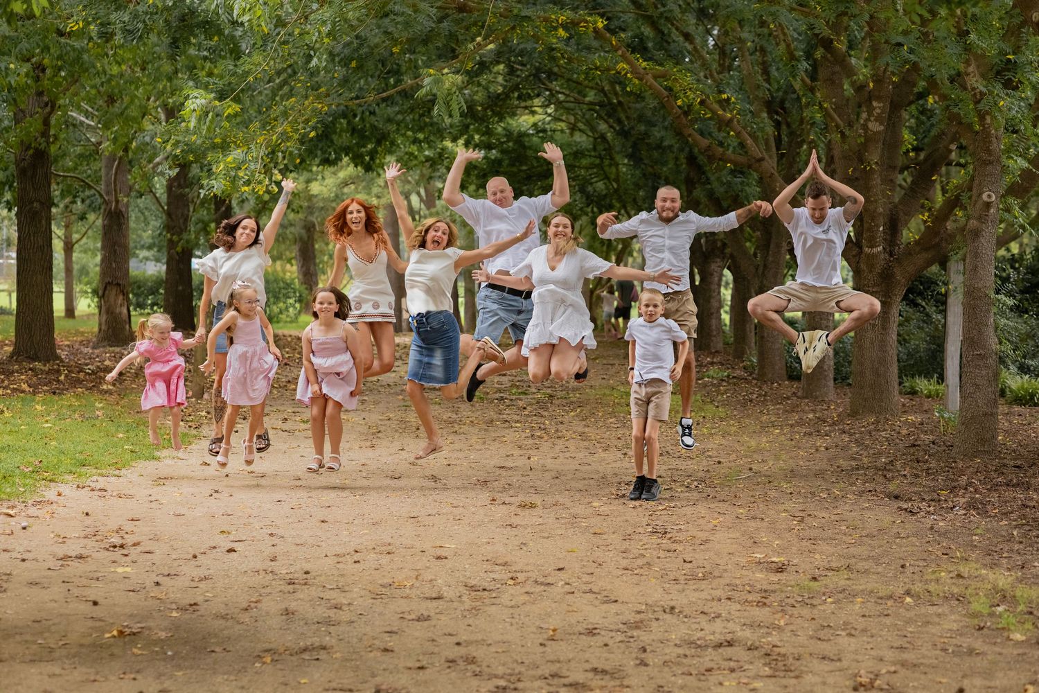 Large extended family jumping joyfully together on dirt path in green park.