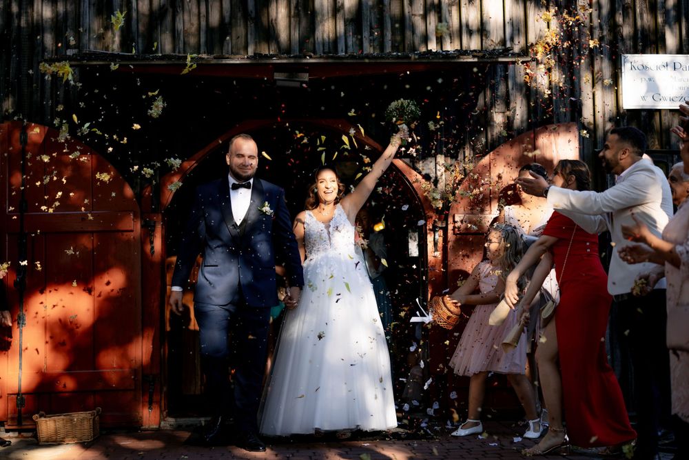 Wedding couple exits venue surrounded by guests throwing confetti in celebration.