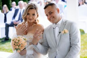A newly married couple shows off their rings while the bride holds a peach-colored bouquet.