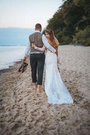 A romantic beach wedding photo of a couple walking barefoot along the shoreline.
