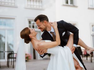 A couple in wedding attire performs a romantic dip dance move against a white building backdrop.