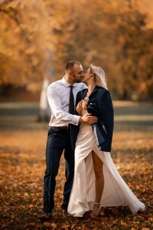 Romantic autumn wedding photo with couple embracing among fallen orange leaves.
