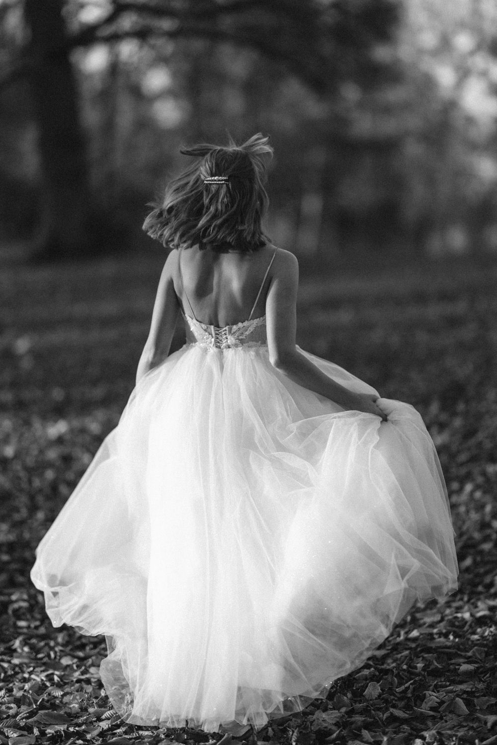Back view of bride in flowing white dress twirling in a forest setting.