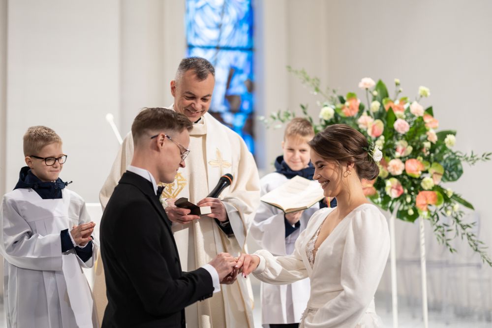 A traditional wedding ceremony taking place in a church with a beautiful floral arrangement in the background.