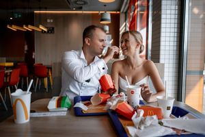 Two people share a meal and laugh together while dining at a casual restaurant with fast food on their table.
