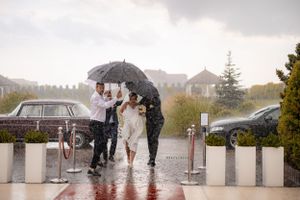 Wedding party huddles under umbrellas in the rain during an outdoor ceremony.