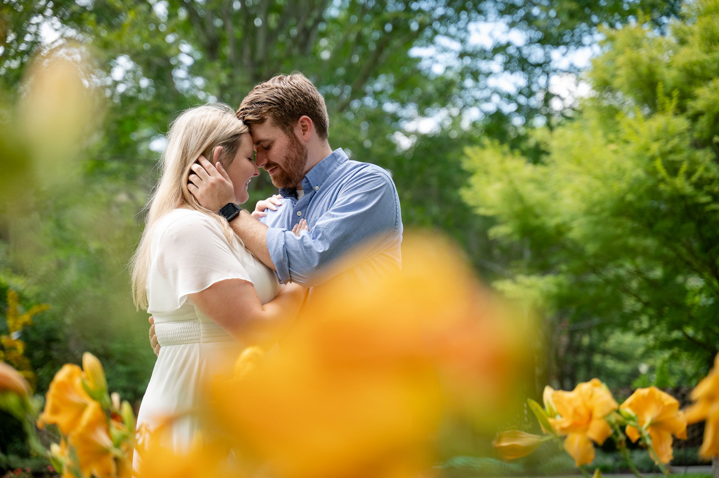 Couple sharing a romantic moment in a lush garden surrounded by vibrant yellow flowers.