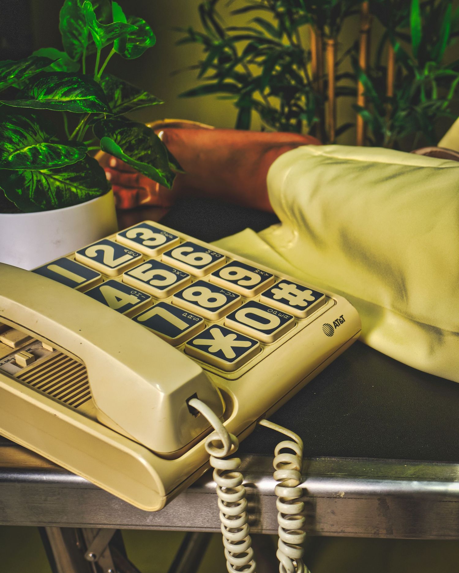Vintage beige telephone with push buttons next to indoor plants in dim lighting.