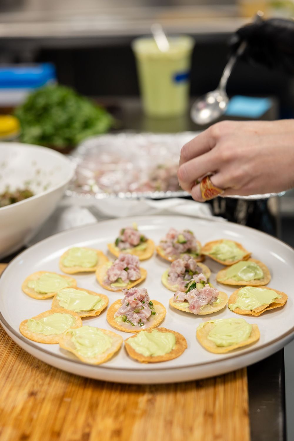 Hand preparing appetizers with tuna or seafood topping on small round crackers arranged on a white plate.