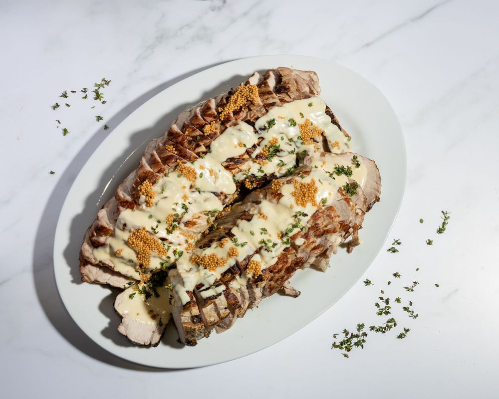Grilled chicken breast topped with melted cheese and herbs served on a white oval plate.
