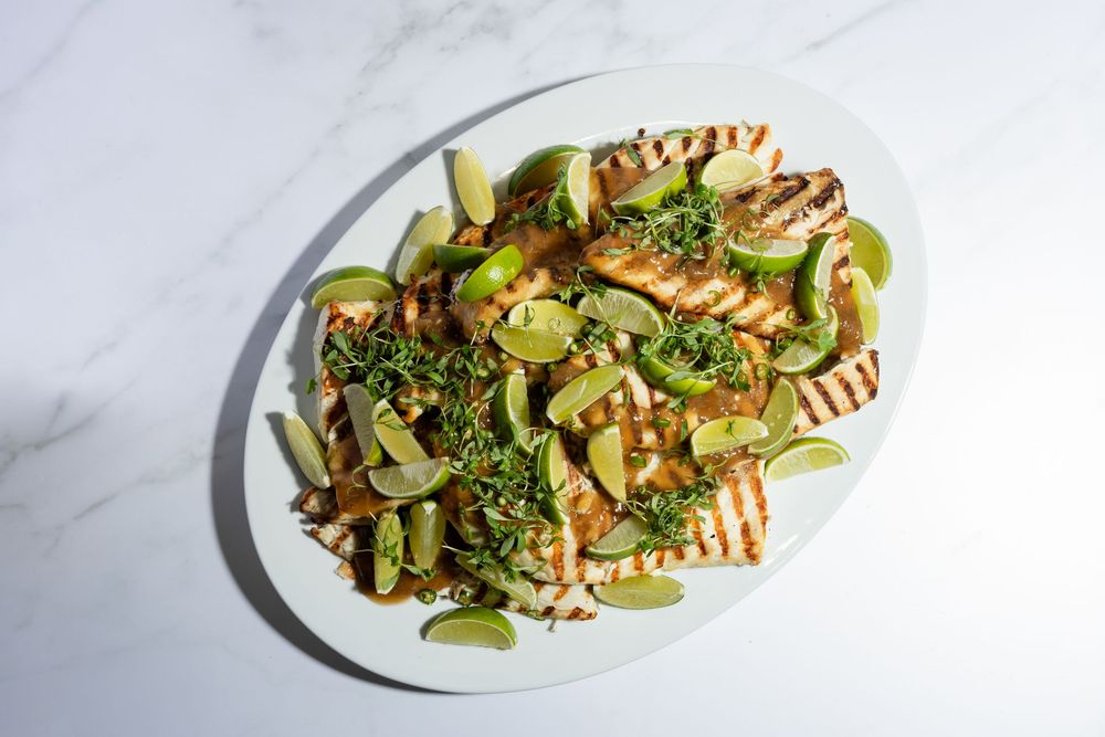 Grilled halloumi cheese salad with avocado slices and herbs served on a white plate against marble background.
