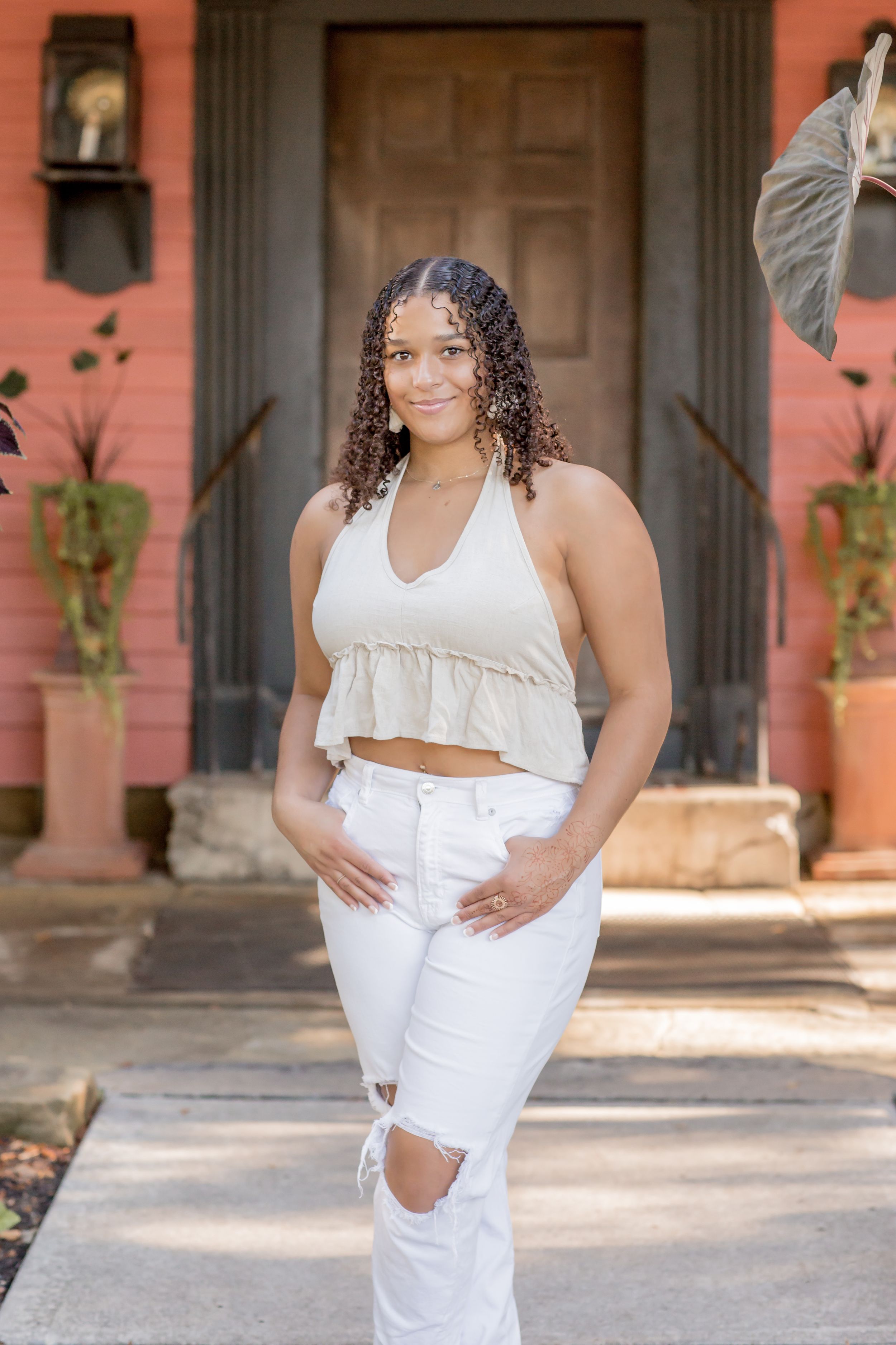 Confident young woman in beige crop top and white ripped jeans posing outside a pink building.