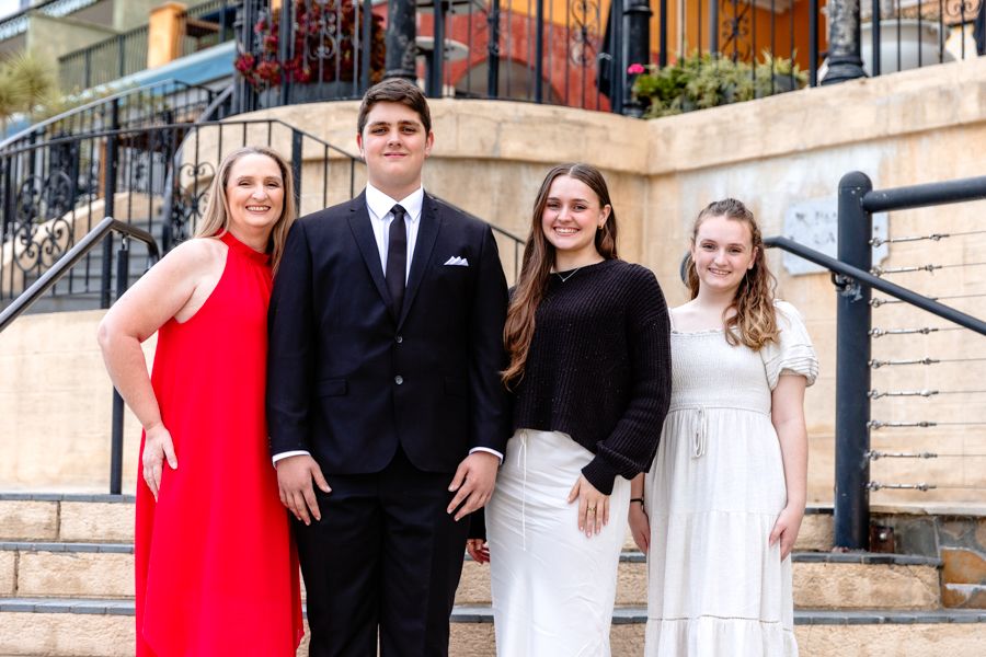 Four formally dressed young adults smiling together on outdoor steps at a special occasion.
