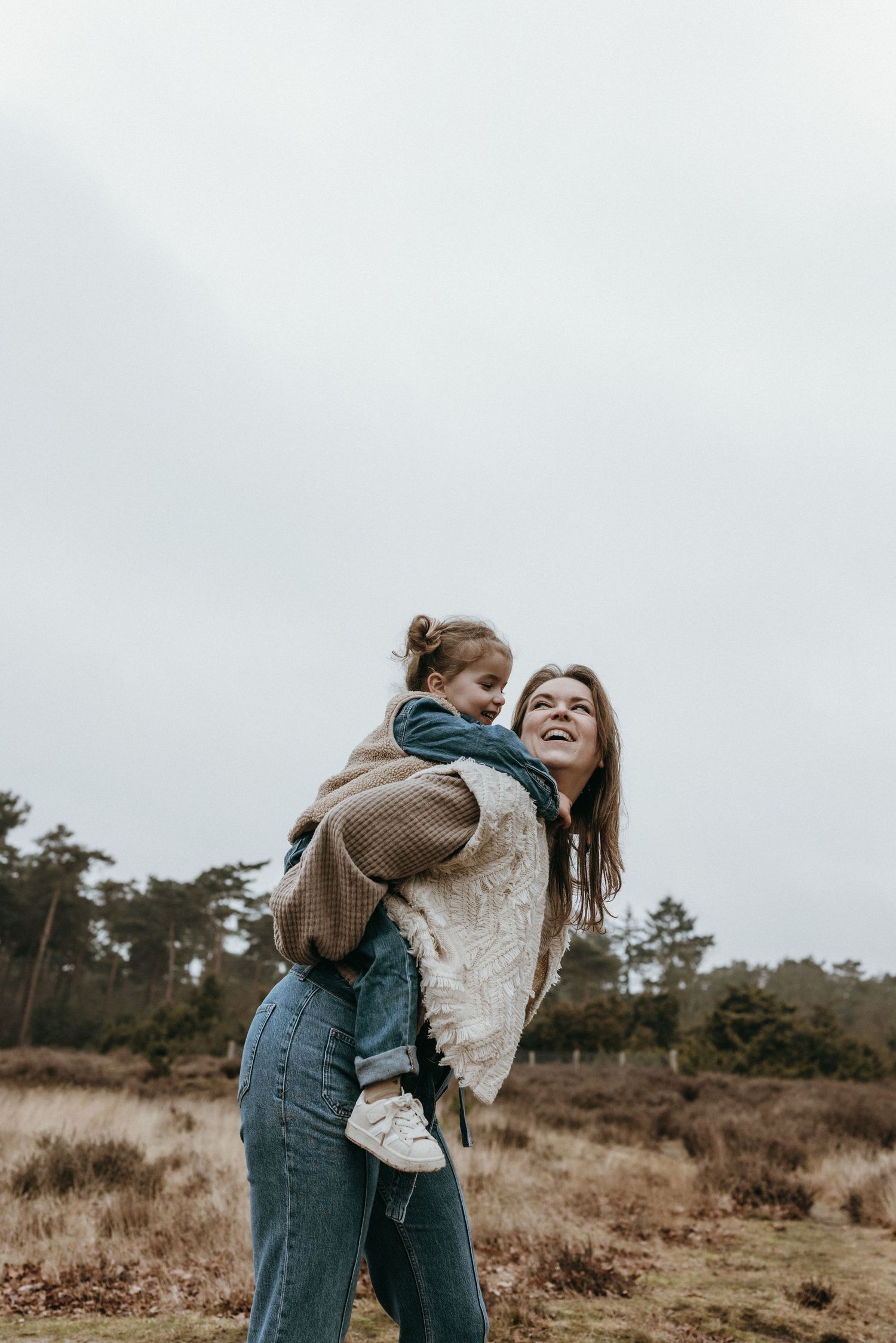 Playful couple embracing in rustic field during overcast day.