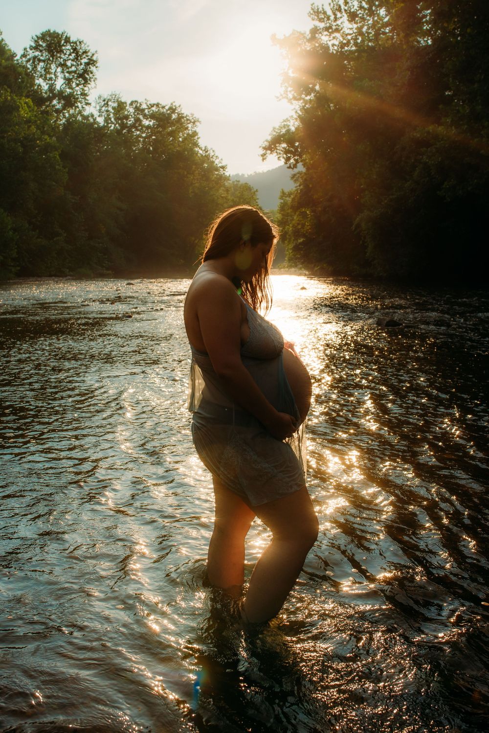 Silhouetted figures embrace in a flowing river at sunset as golden light sparkles on the rippling water.
